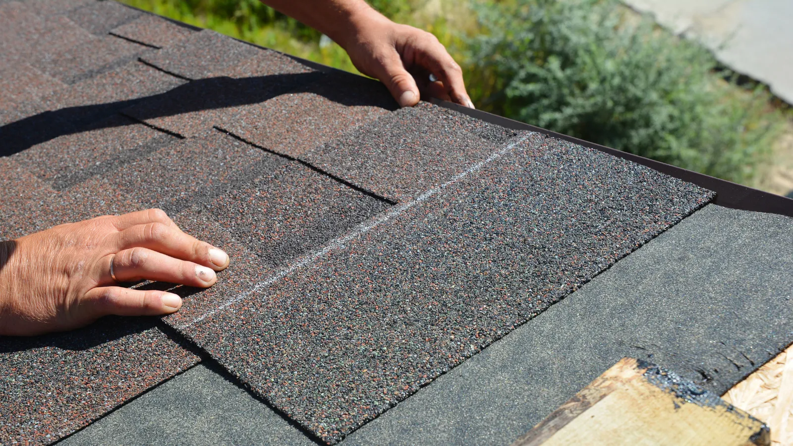 Hands of a roofer laying courses of asphalt shingles at a roof edge