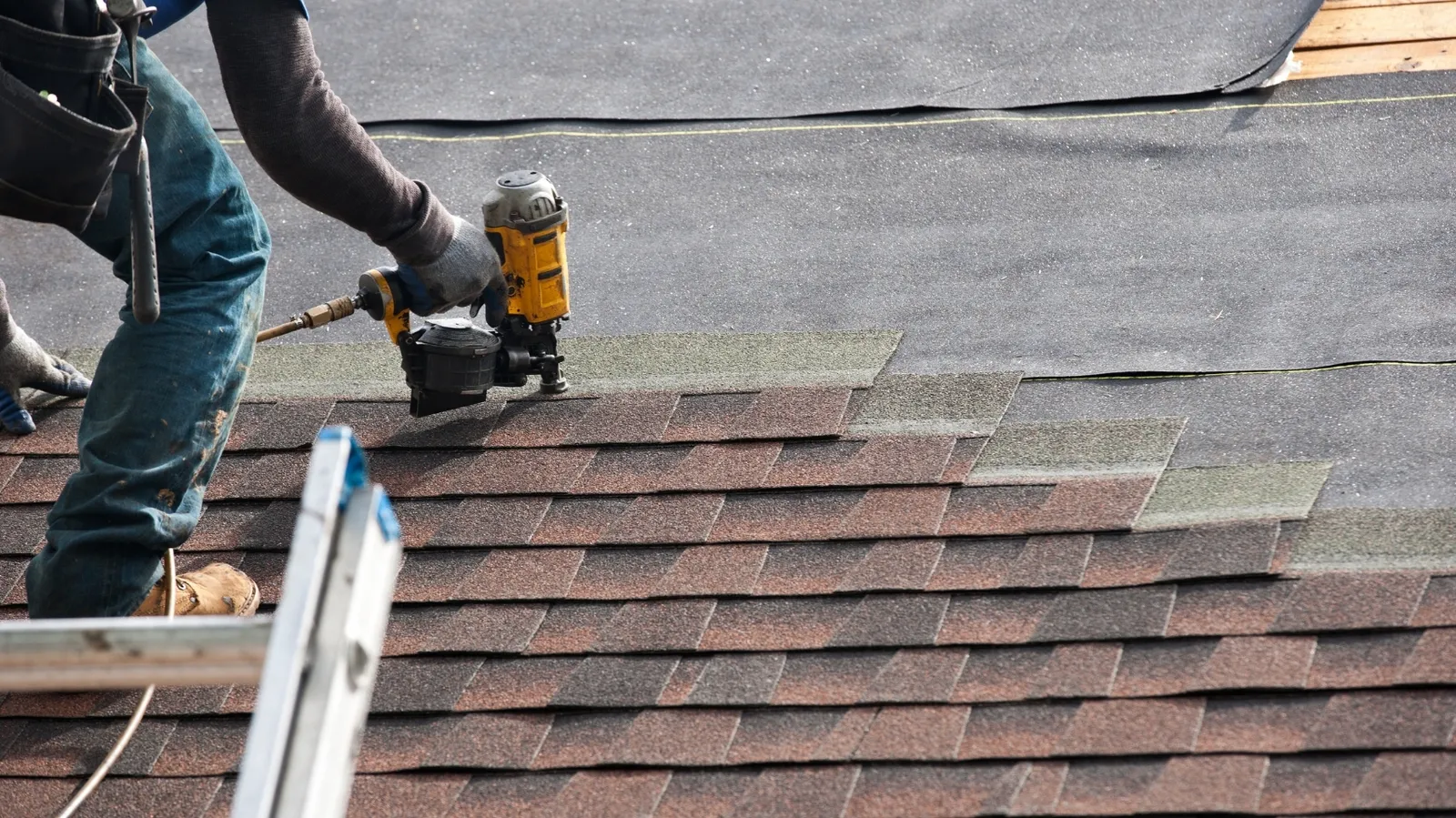 A roofer fastening asphalt shingles with a pneumatic coil nailer