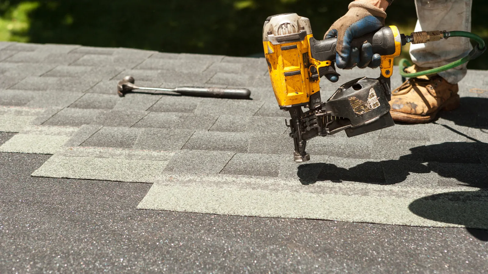 Shingles being nailed by a roofer with a hammer resting nearby