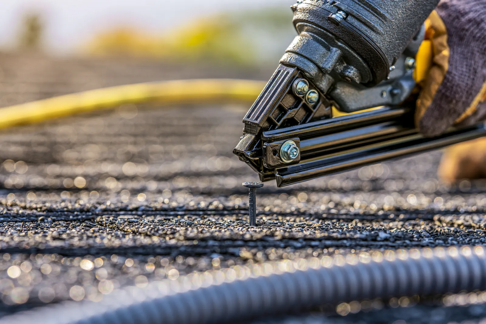 A roofer drives a nail into asphalt shingles with a nail gun